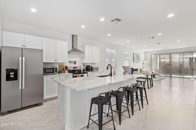 kitchen with stainless steel appliances, a center island with sink, sink, white cabinets, and wall chimney range hood