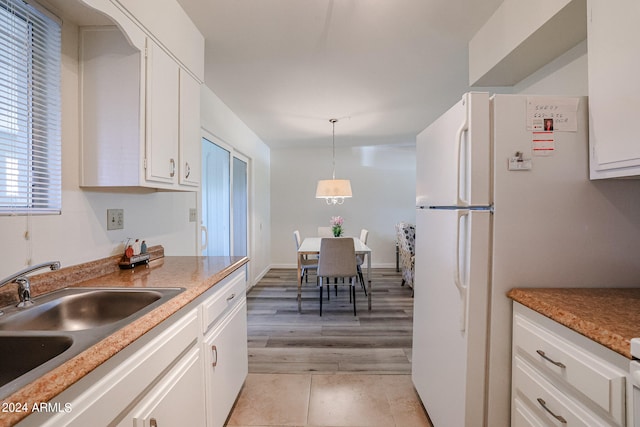 kitchen with sink, light tile patterned floors, white refrigerator, decorative light fixtures, and white cabinetry