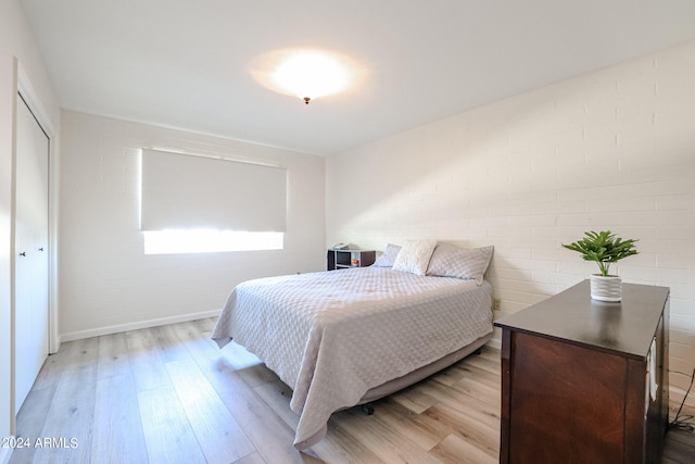 bedroom featuring a closet, light hardwood / wood-style floors, and brick wall