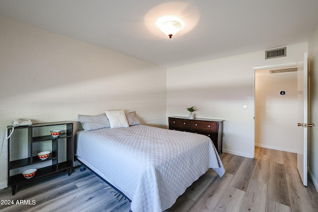 bedroom featuring light wood-type flooring and brick wall