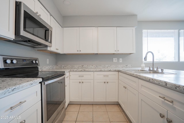 kitchen with light stone counters, light tile patterned flooring, a sink, stainless steel appliances, and white cabinetry