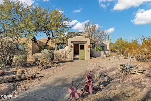 pueblo-style home with a gate, fence, and stucco siding