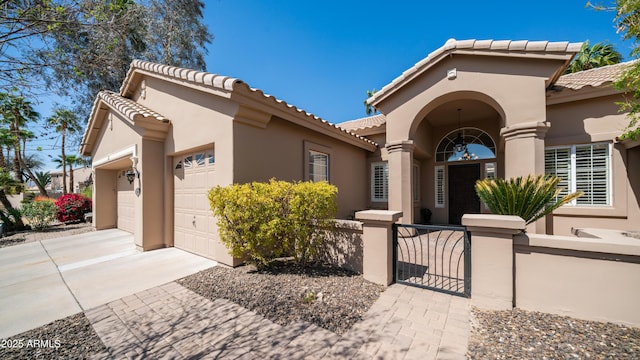 mediterranean / spanish-style home featuring stucco siding, driveway, a gate, a fenced front yard, and a garage