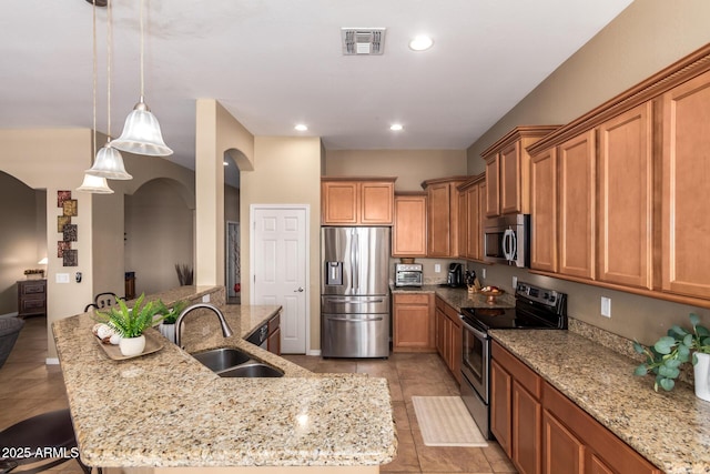 kitchen with stainless steel appliances, a sink, arched walkways, light tile patterned flooring, and brown cabinets