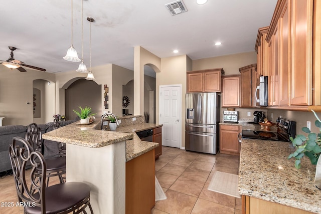 kitchen featuring appliances with stainless steel finishes, open floor plan, arched walkways, a breakfast bar area, and light stone counters