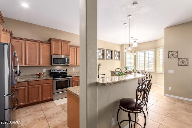 kitchen with stainless steel appliances, brown cabinets, a breakfast bar, light tile patterned floors, and light stone countertops