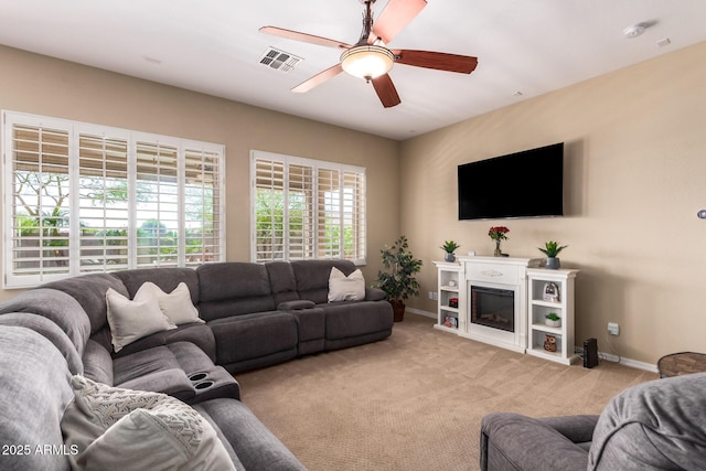 living room with baseboards, light carpet, a ceiling fan, and a glass covered fireplace