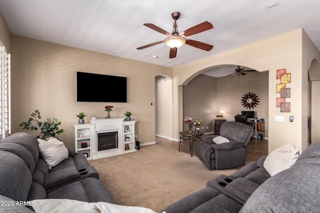 living area featuring arched walkways, ceiling fan, baseboards, and carpet floors