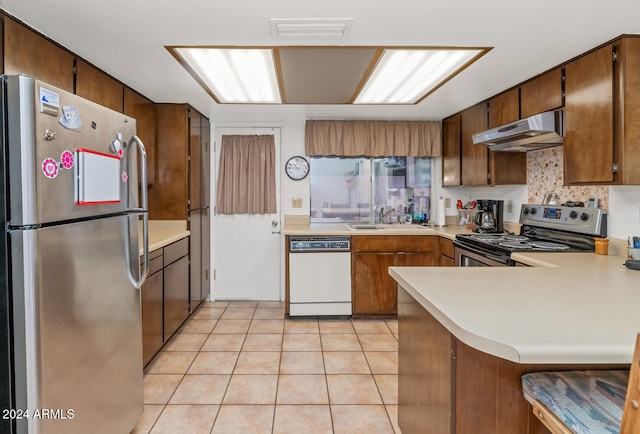 kitchen with kitchen peninsula, appliances with stainless steel finishes, tasteful backsplash, sink, and light tile patterned floors