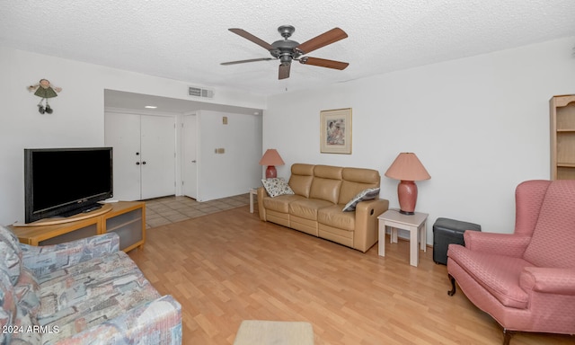 living room featuring ceiling fan, light hardwood / wood-style flooring, and a textured ceiling