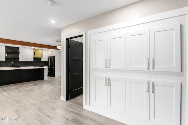 kitchen featuring sink, tasteful backsplash, light hardwood / wood-style floors, white cabinets, and black fridge