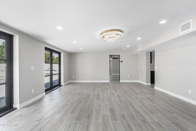 spare room featuring french doors, a notable chandelier, and light wood-type flooring