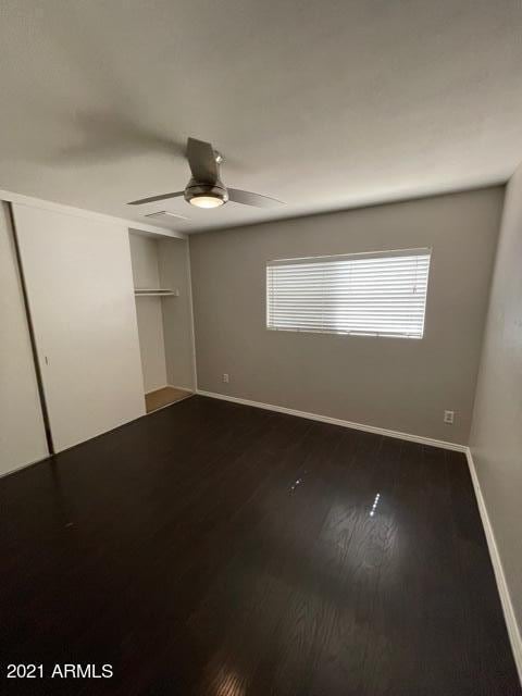 unfurnished bedroom with dark wood-style floors, ceiling fan, baseboards, and a closet