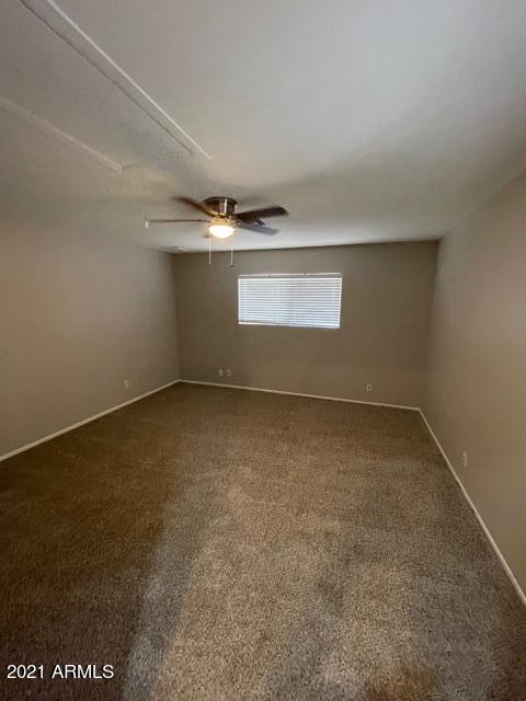 spare room featuring attic access, dark carpet, baseboards, and a ceiling fan