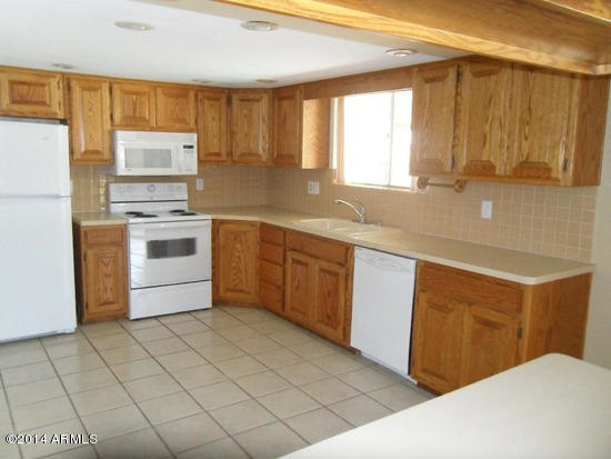 kitchen with white appliances, brown cabinetry, a sink, and light countertops