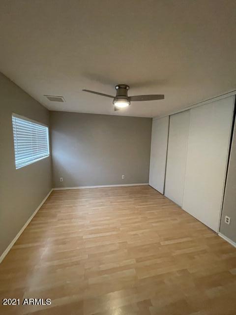 unfurnished bedroom with light wood finished floors, ceiling fan, visible vents, and a closet