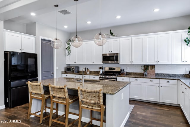 kitchen with dark stone counters, dark wood-style floors, a sink, stainless steel appliances, and white cabinets
