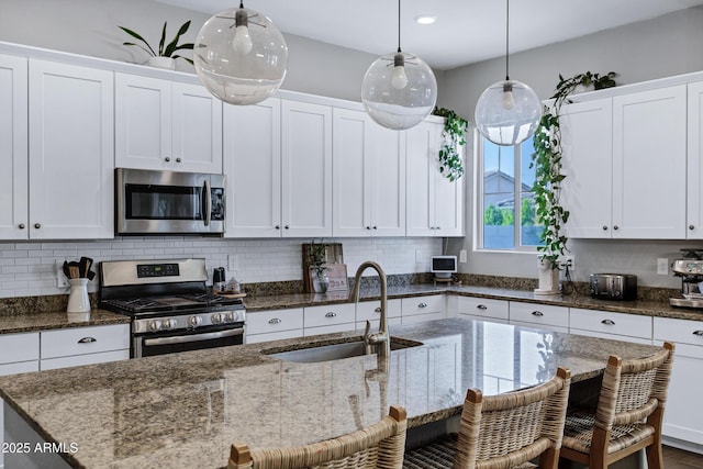 kitchen featuring an island with sink, a breakfast bar, stainless steel appliances, decorative light fixtures, and a sink