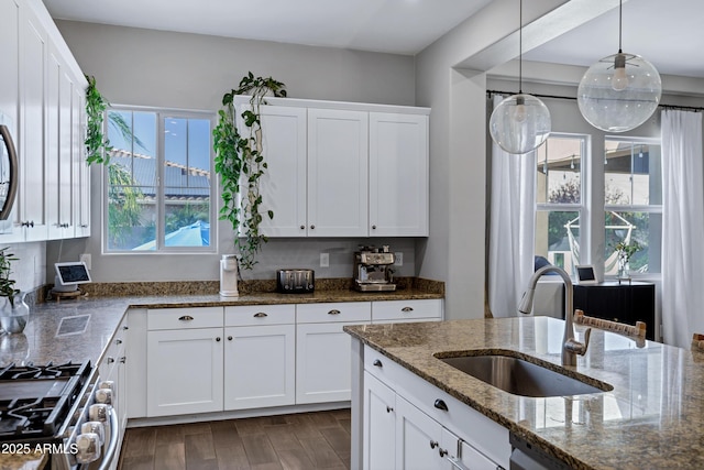 kitchen with dark stone countertops, white cabinets, a sink, gas stove, and decorative light fixtures
