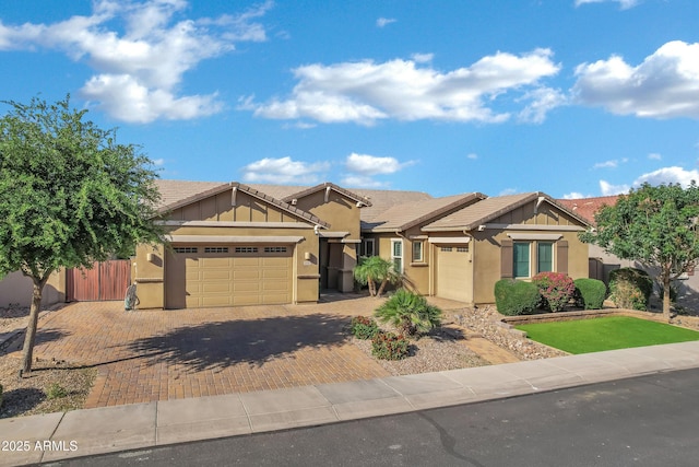 view of front of property featuring fence, a tiled roof, decorative driveway, stucco siding, and a garage