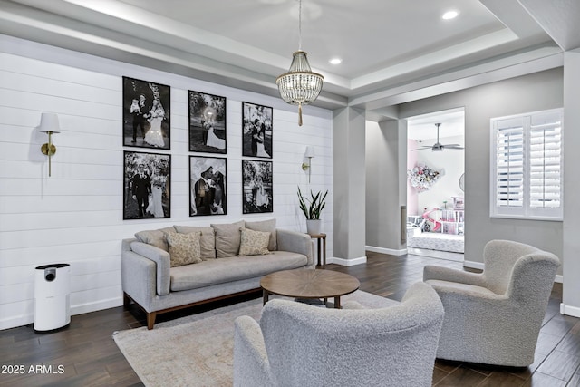 living area with recessed lighting, ceiling fan, dark wood-type flooring, a tray ceiling, and baseboards