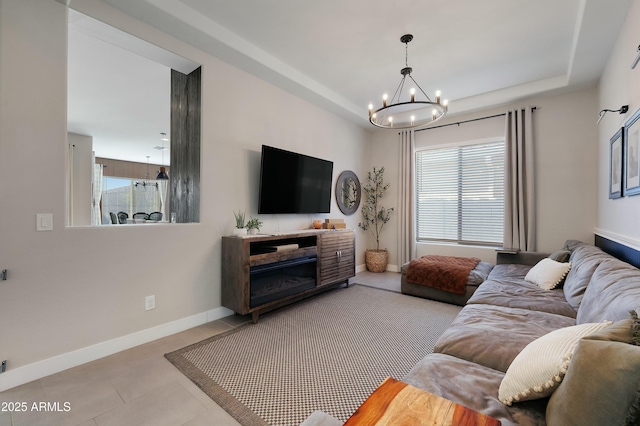 living room with tile patterned flooring, a raised ceiling, a notable chandelier, and baseboards