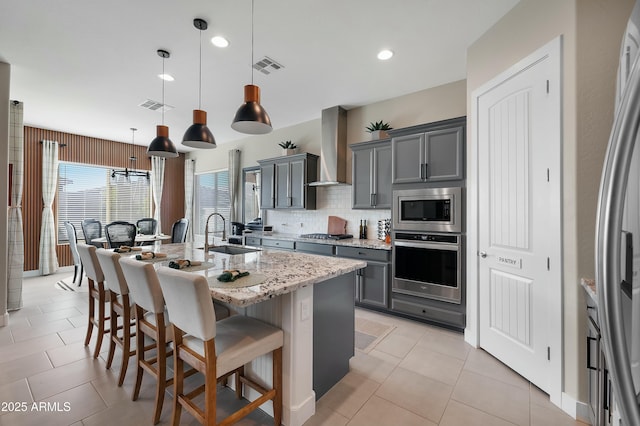 kitchen featuring visible vents, wall chimney exhaust hood, appliances with stainless steel finishes, gray cabinets, and a sink