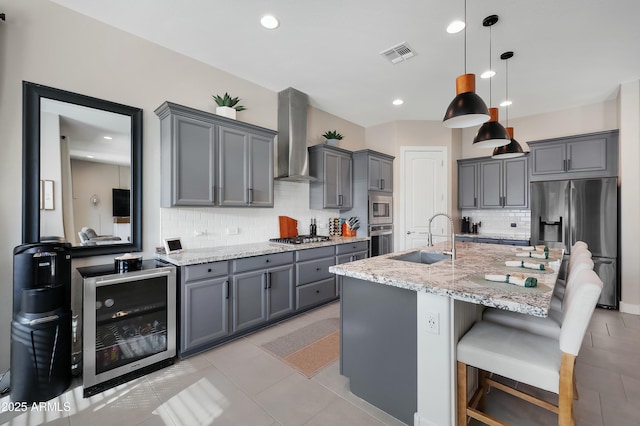 kitchen featuring wine cooler, stainless steel appliances, a sink, visible vents, and wall chimney range hood