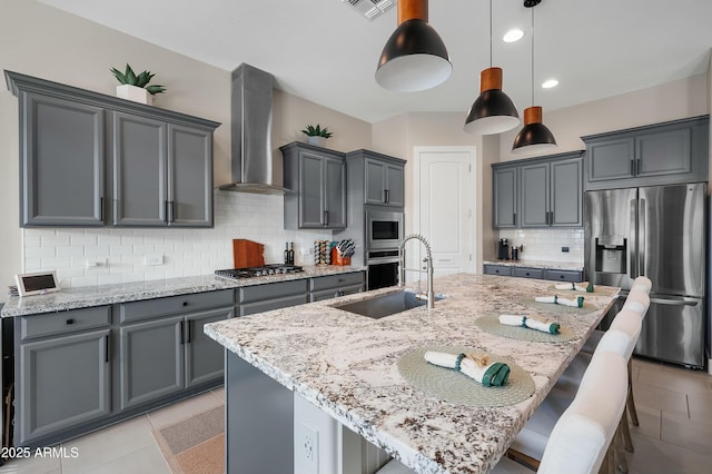 kitchen featuring light stone counters, stainless steel appliances, a sink, a kitchen breakfast bar, and wall chimney range hood