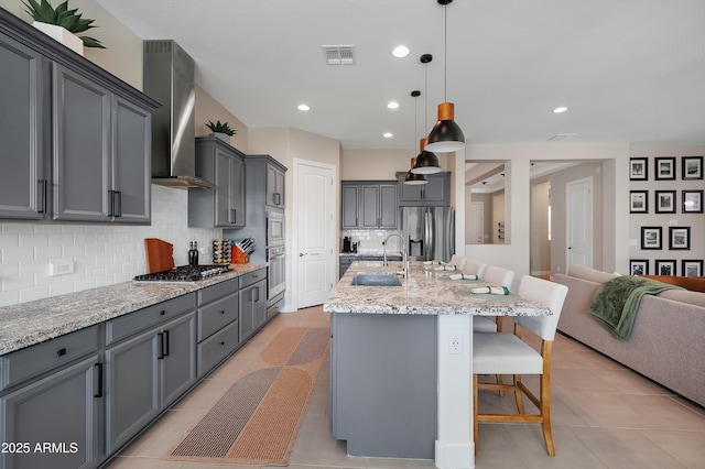 kitchen featuring stainless steel appliances, a sink, visible vents, wall chimney range hood, and a kitchen bar