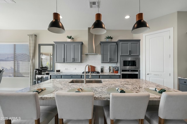 kitchen with stainless steel appliances, gray cabinetry, a sink, and wall chimney exhaust hood