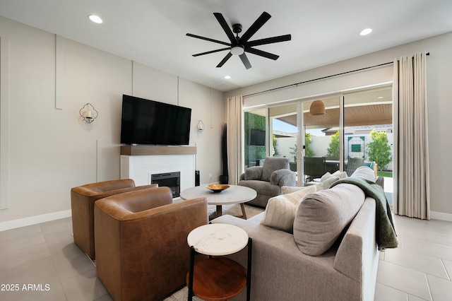 living area with a glass covered fireplace, ceiling fan, baseboards, and recessed lighting