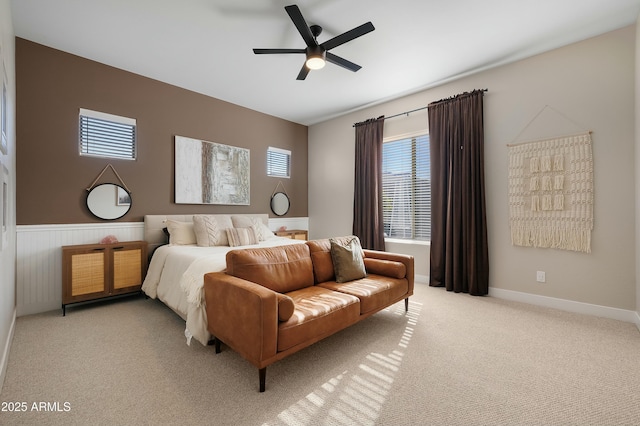 bedroom with a ceiling fan, a wainscoted wall, and light carpet