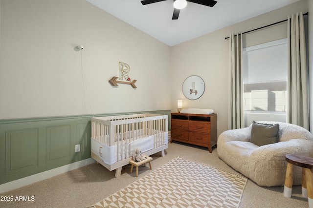 bedroom with light carpet, wainscoting, a ceiling fan, and a decorative wall