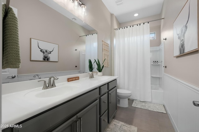 full bathroom with a wainscoted wall, double vanity, a sink, and toilet