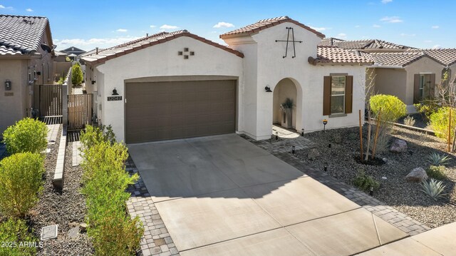 mediterranean / spanish house with a tile roof, stucco siding, a gate, a garage, and driveway