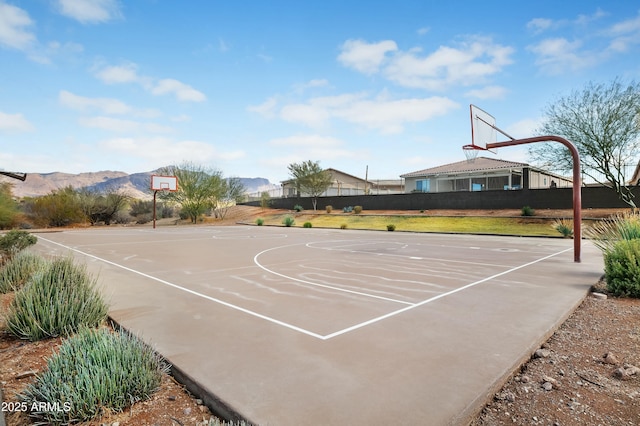 view of basketball court featuring community basketball court, a mountain view, fence, and a yard