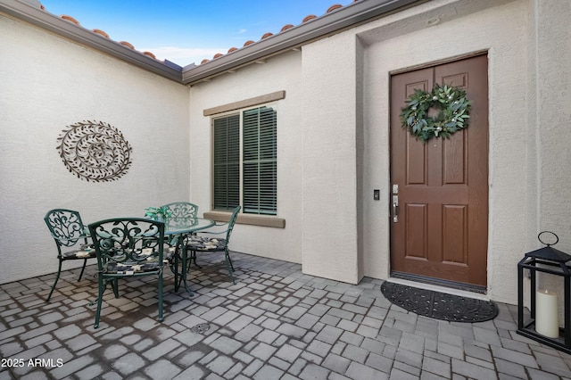 view of exterior entry with a patio area, a tile roof, outdoor dining area, and stucco siding