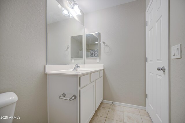 bathroom with baseboards, toilet, a textured wall, vanity, and tile patterned floors