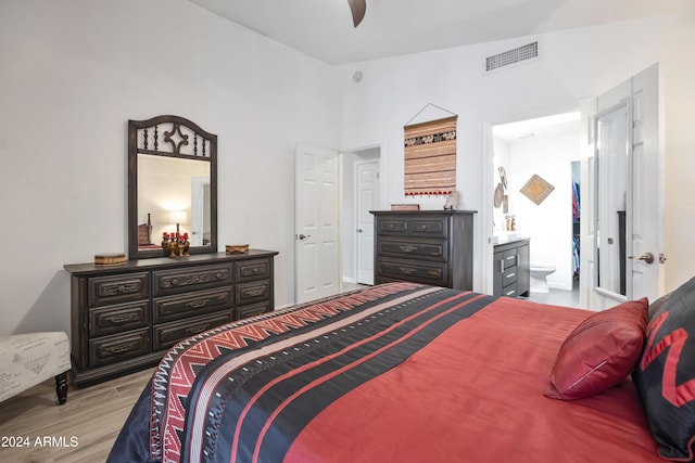 bedroom featuring light wood-type flooring, connected bathroom, vaulted ceiling, and ceiling fan