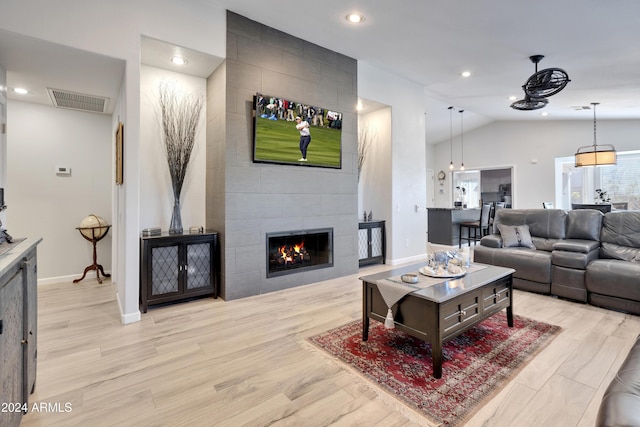 living room featuring lofted ceiling, light hardwood / wood-style flooring, and a tiled fireplace