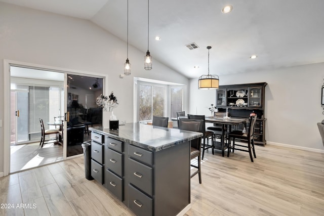 kitchen featuring hanging light fixtures, a kitchen breakfast bar, dark stone countertops, vaulted ceiling, and gray cabinets