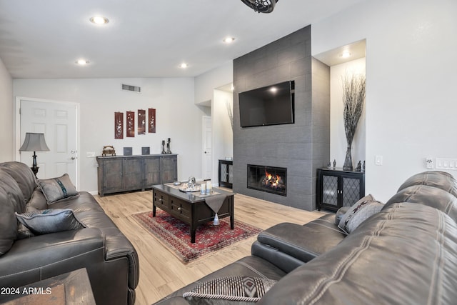 living room featuring light hardwood / wood-style floors, lofted ceiling, and a tile fireplace