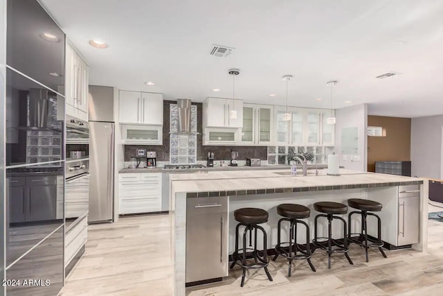 kitchen with a center island with sink, white cabinetry, decorative light fixtures, and wall chimney exhaust hood