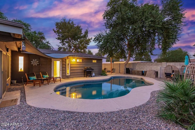 pool at dusk featuring area for grilling and a patio