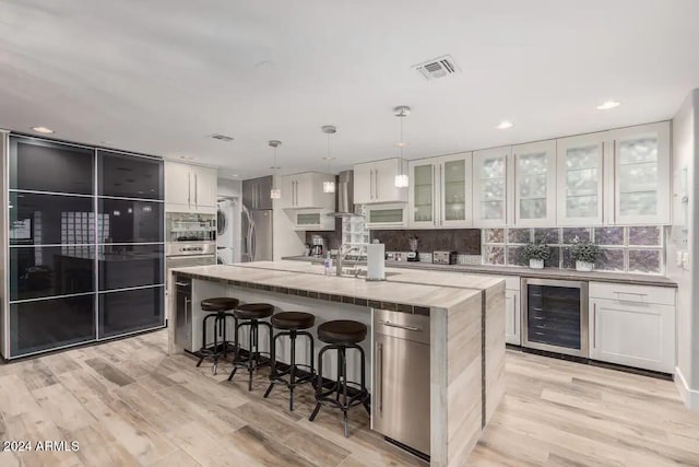 kitchen with a kitchen island with sink, decorative light fixtures, light wood-type flooring, and beverage cooler