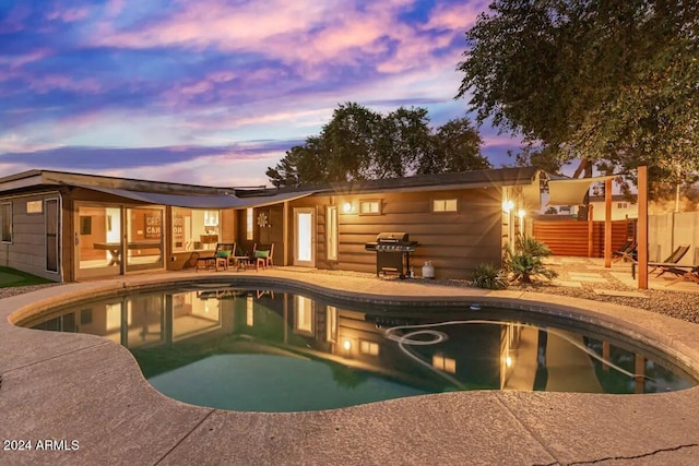 pool at dusk featuring a patio and a grill