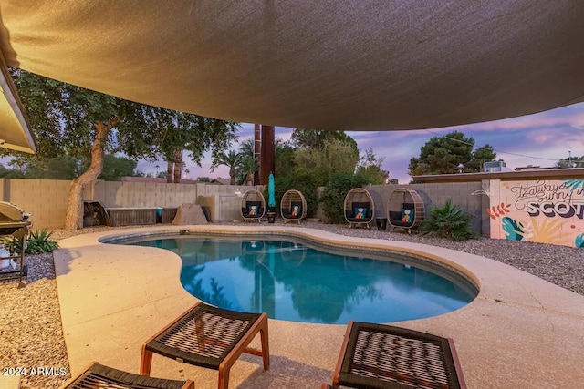 pool at dusk with a patio and grilling area