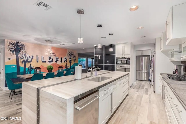 kitchen featuring light hardwood / wood-style flooring, a center island with sink, white cabinets, decorative light fixtures, and appliances with stainless steel finishes