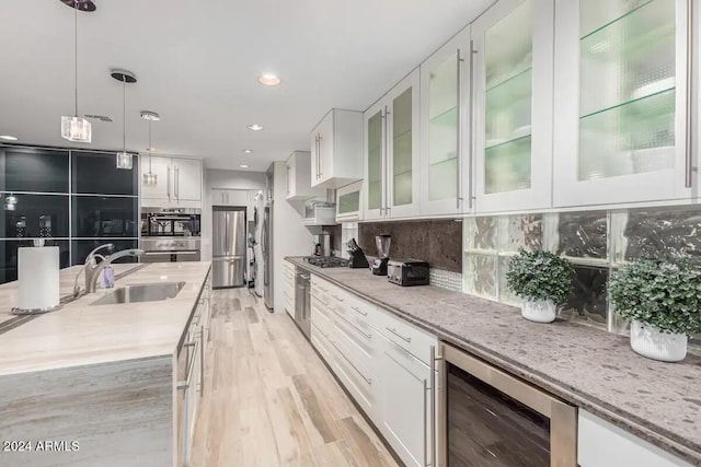 kitchen with wine cooler, tasteful backsplash, white cabinetry, light stone countertops, and sink